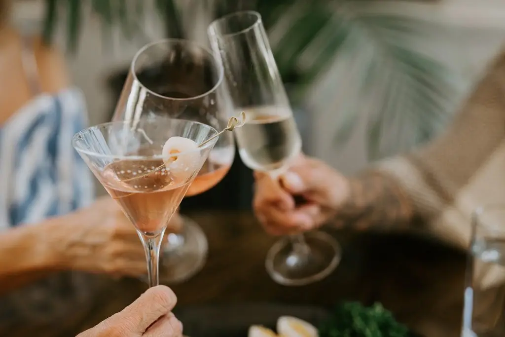 A group of three toast a cocktail, a champagne and a glass of wine.