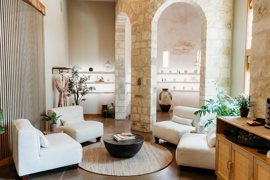 The Hill Country Herb Garden Spa Retail space is light and airy, with exposed white brick archways. The space features shelving and racks of retail and a seating area for four.